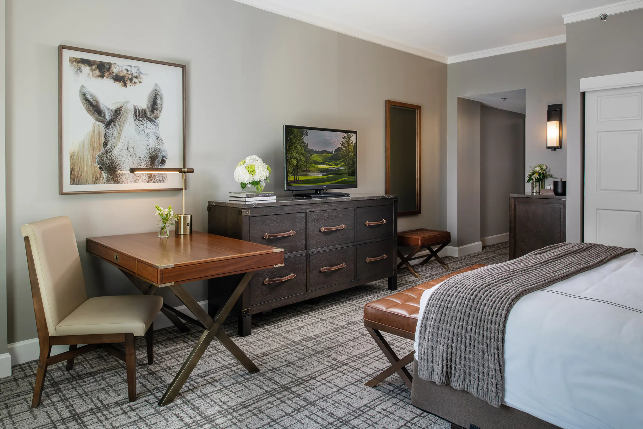 Close-up view of Deluxe King room with tufted amber headboard, walnut nightstand, table lamp, grey upholstered armchair with orange accent pillow, and patterned carpet
