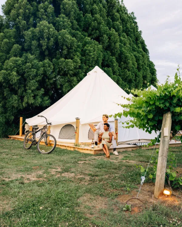 A large white tent is set up outdoors on a grassy area surrounded by trees.