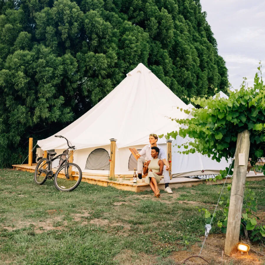 A large white tent is set up outdoors on a grassy area surrounded by trees.