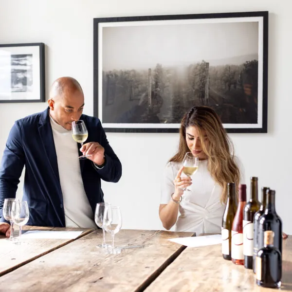 A man and a woman are seated at a rustic wooden table, each holding a glass of wine.