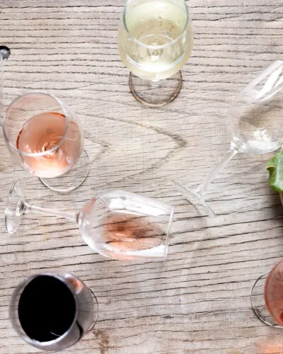 An overhead shot of a wooden table with several glasses of red, white, and rosé wine arranged around a wine carafe.