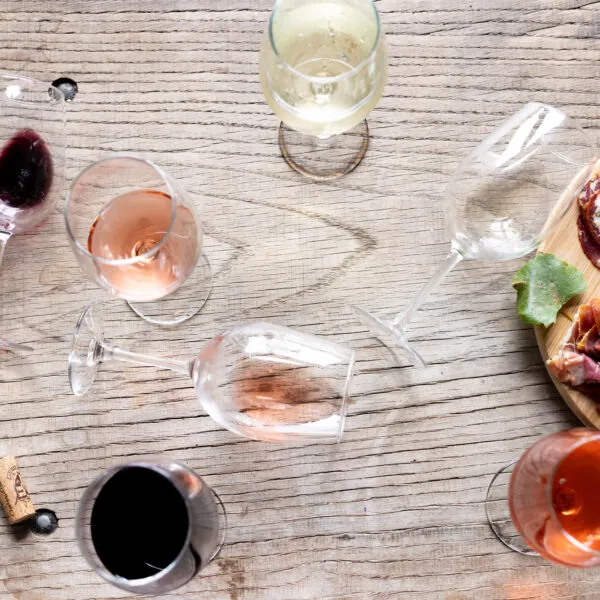 An overhead shot of a wooden table with several glasses of red, white, and rosé wine arranged around a wine carafe.