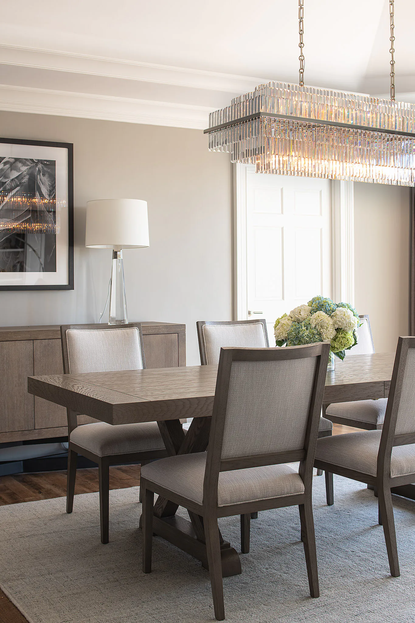 Suite dining area with wooden table, upholstered chairs, crystal chandelier, framed artwork, and large windows with natural light