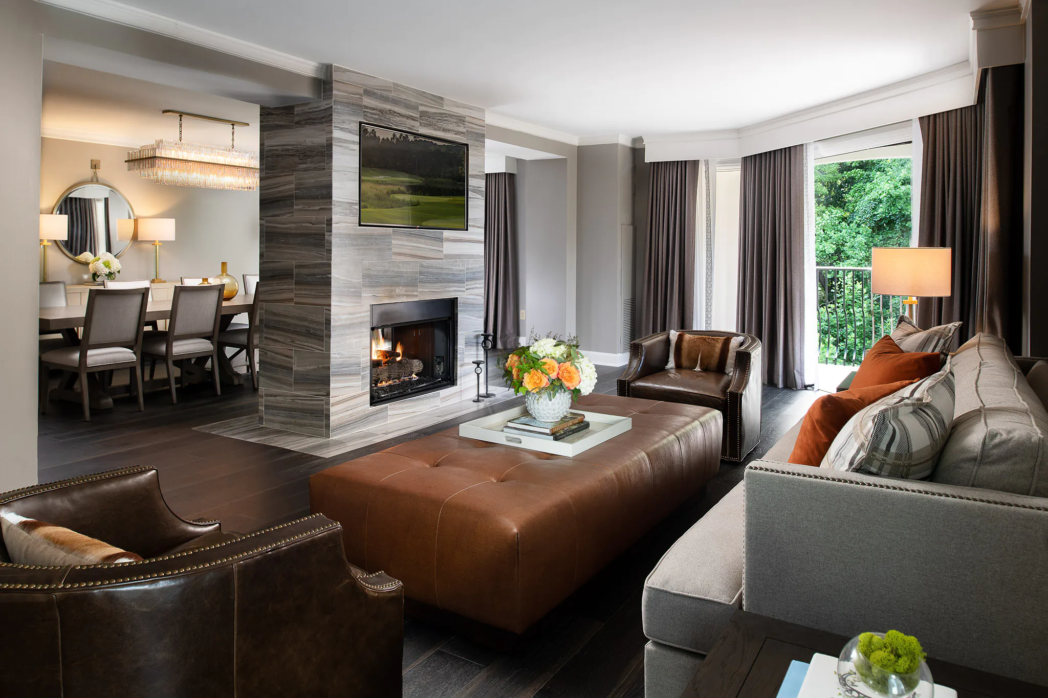 Suite living room with leather sofa, grey upholstered seating, stone fireplace, flat-screen TV, and floor-to-ceiling curtains