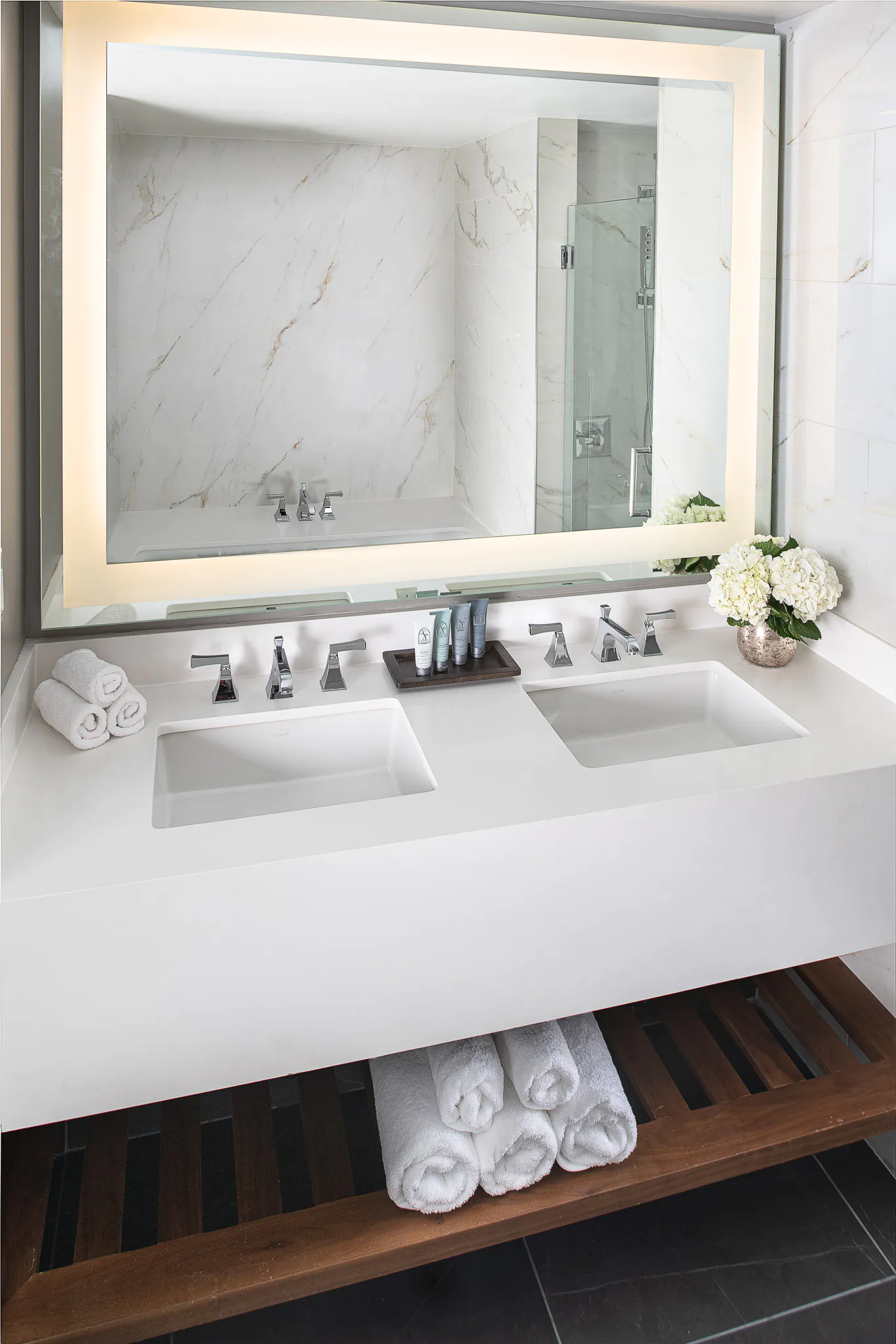 Marble bathroom vanity with undermount sink, chrome fixtures, illuminated mirror, and fresh white floral arrangement