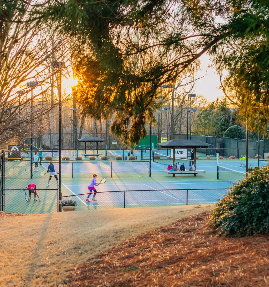 People playing tennis on outdoor courts at sunset