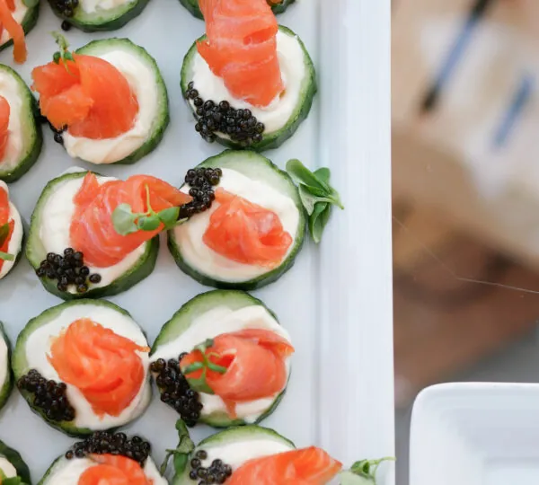 A platter of appetizers made with cucumber slices, cream cheese, smoked salmon, and black caviar.