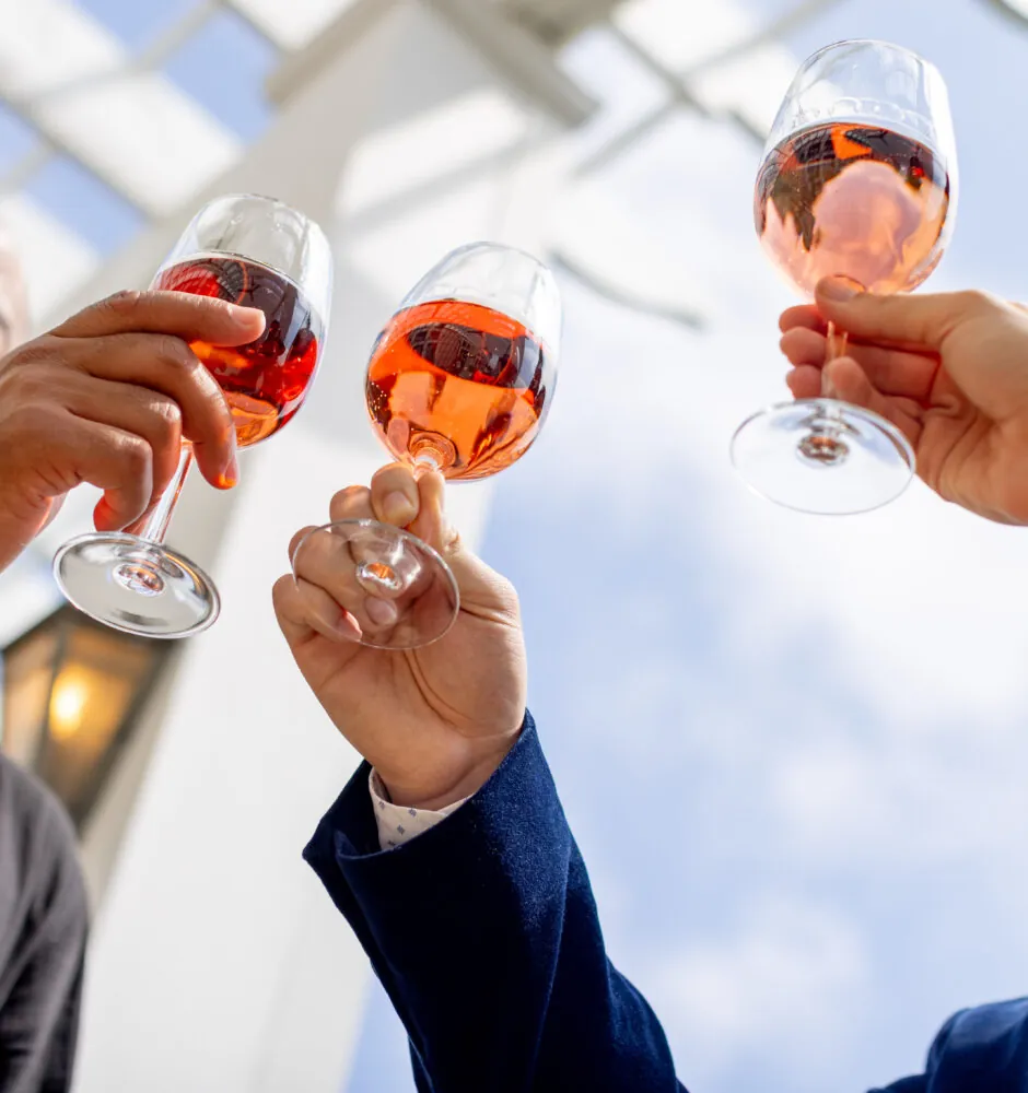 A group of three people cheers with glasses of rosé wine.