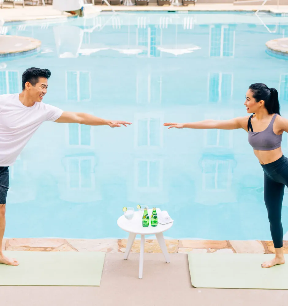 Man and woman doing yoga poses by pool