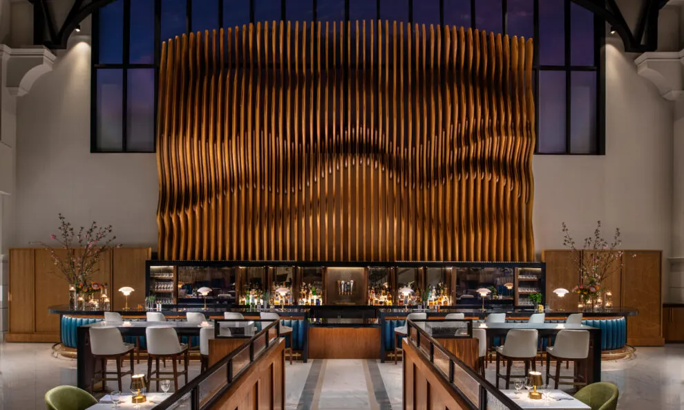 A long, modern dining hall with rows of tables and chairs facing a large, textured wooden wall.