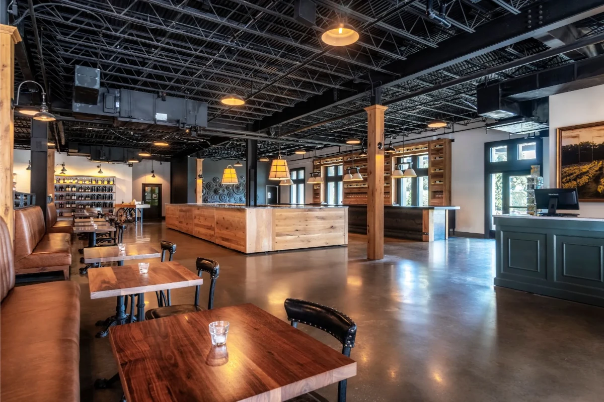 An indoor room with high ceilings, exposed beams, and a concrete floor. There are tables and benches on one side and an empty space that could be used for dancing or mingling.