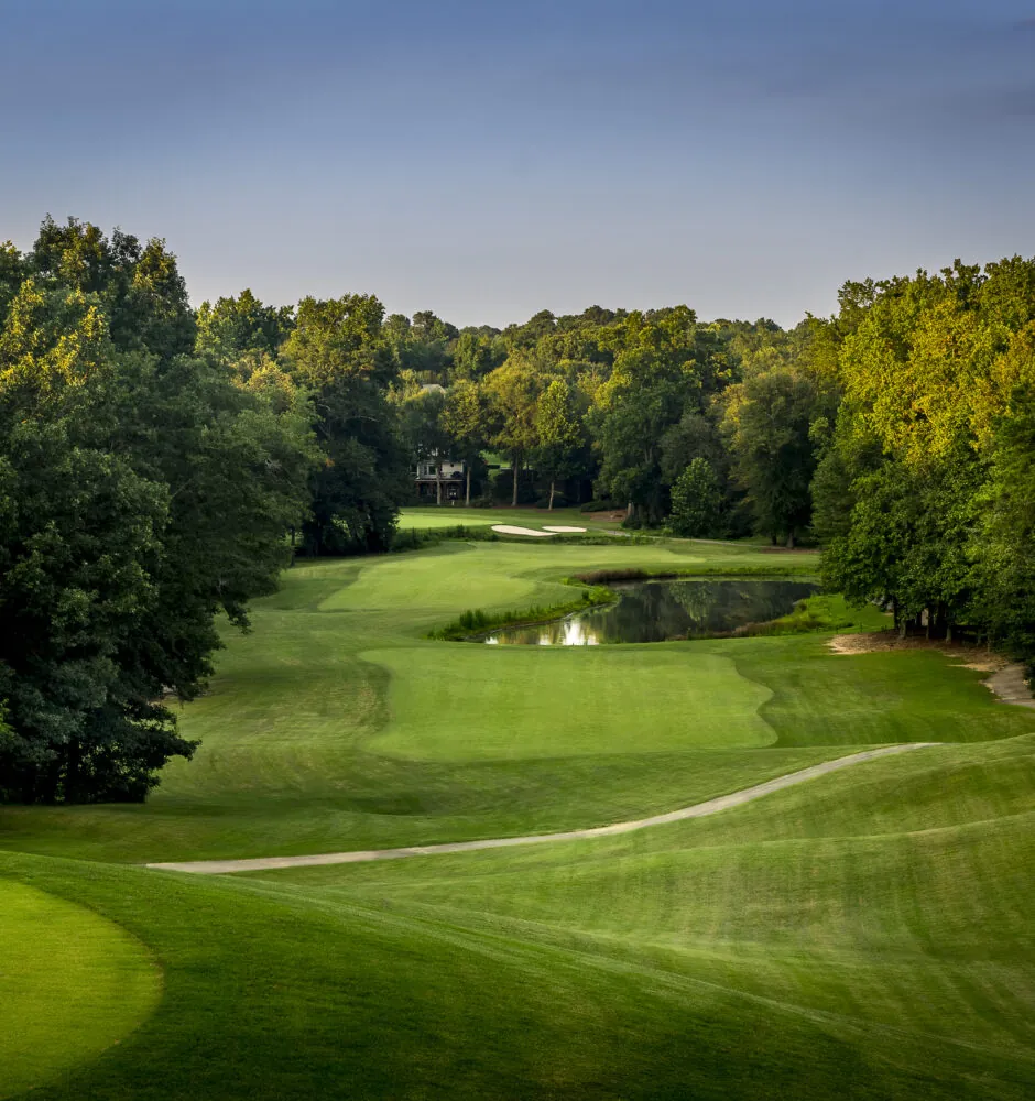 A green golf course with trees and a small pond.