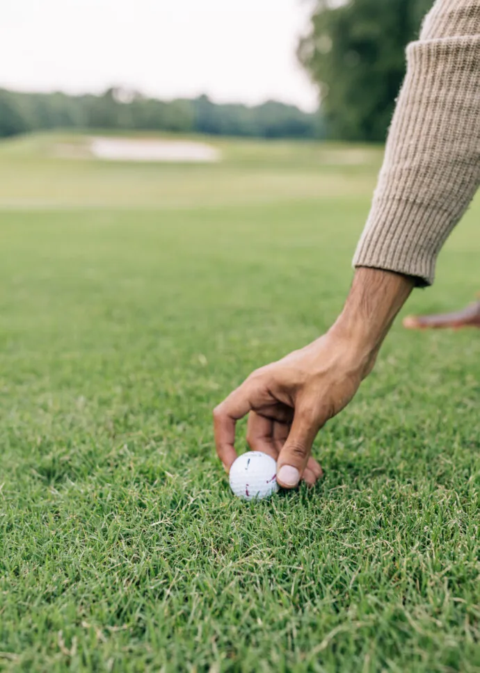 A close-up of a person's hand placing a golf ball on the green grass.