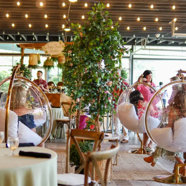 People gathered for an event in a decorated room with large plants and glowing lights.