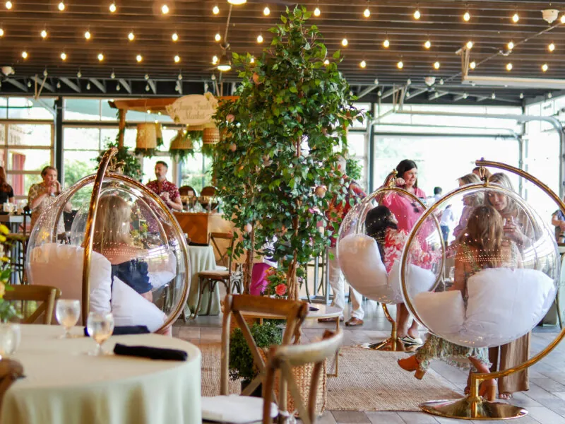 People gathered for an event in a decorated room with large plants and glowing lights.