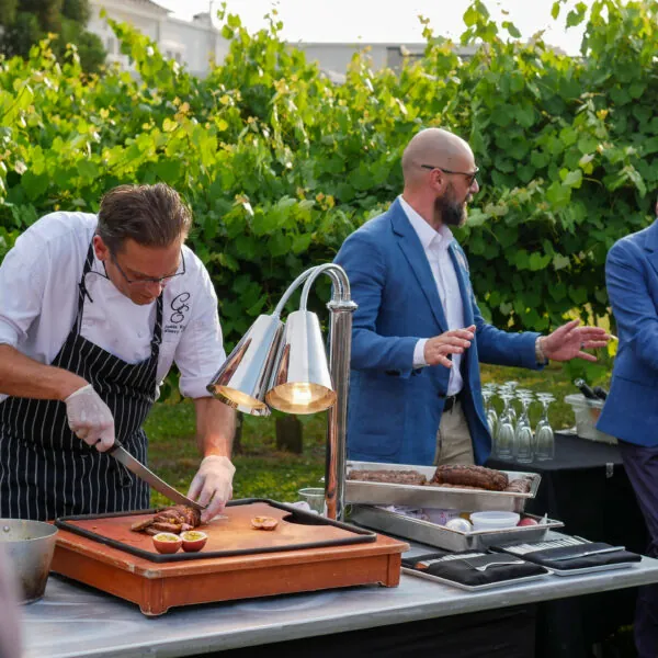 Two chefs preparing food on a grill outdoors for guests.