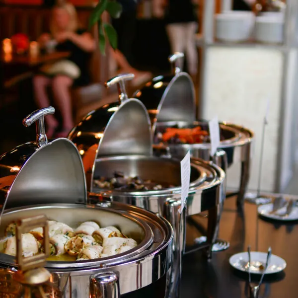 A buffet with several silver chafing dishes and food being served.