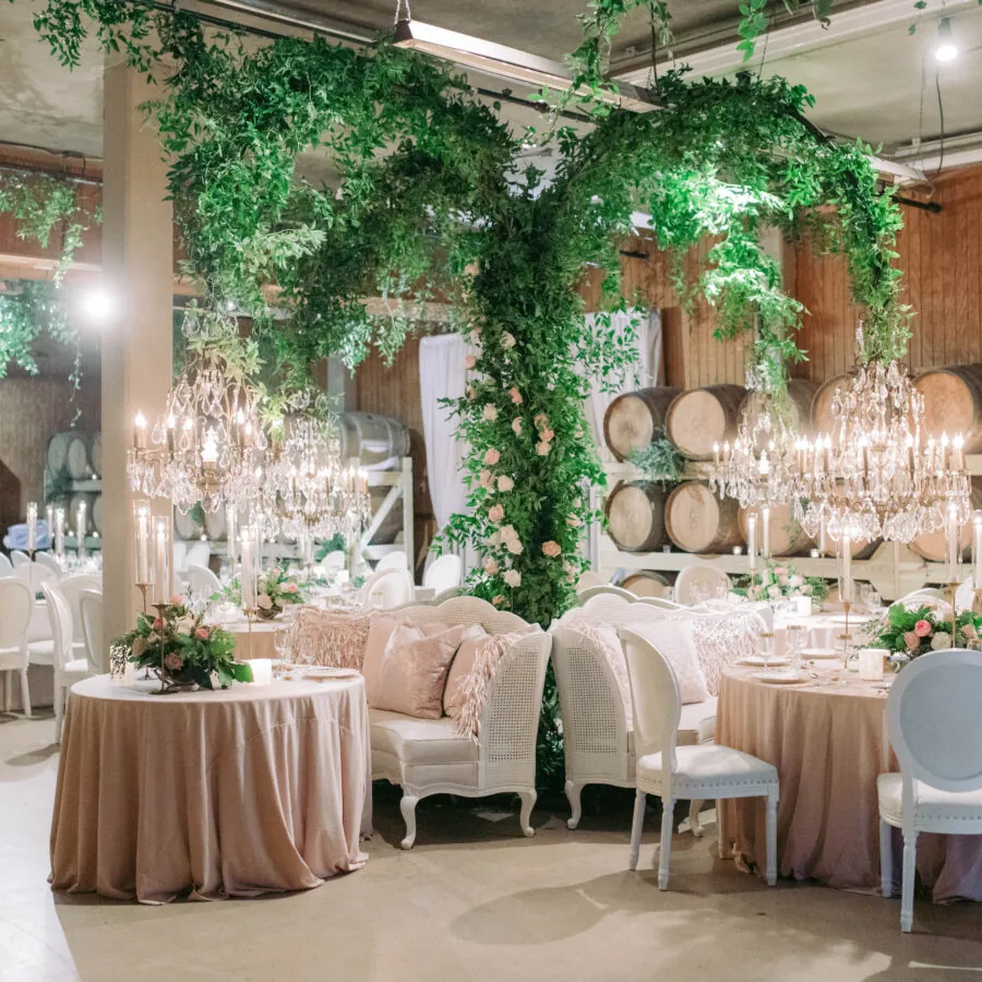 Reception room decorated with lush green vines, barrels, and elegant white furniture.