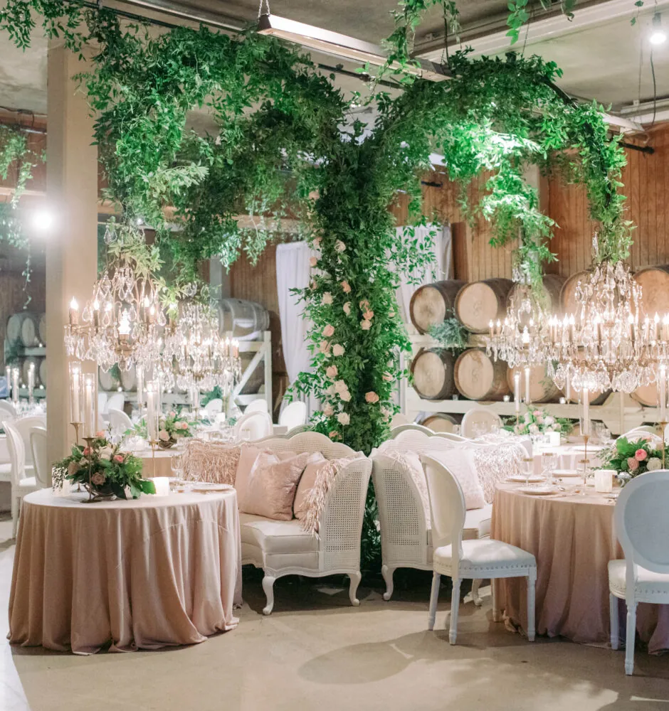 Reception room decorated with lush green vines, barrels, and elegant white furniture.