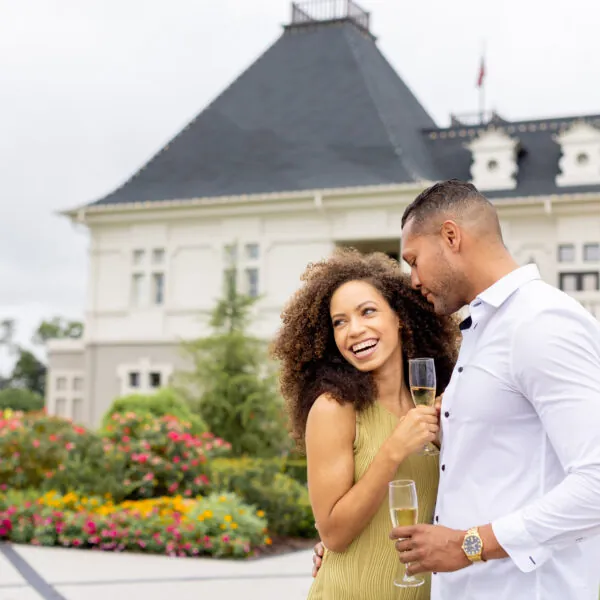 Smiling couple with champagne glasses in front of hotel