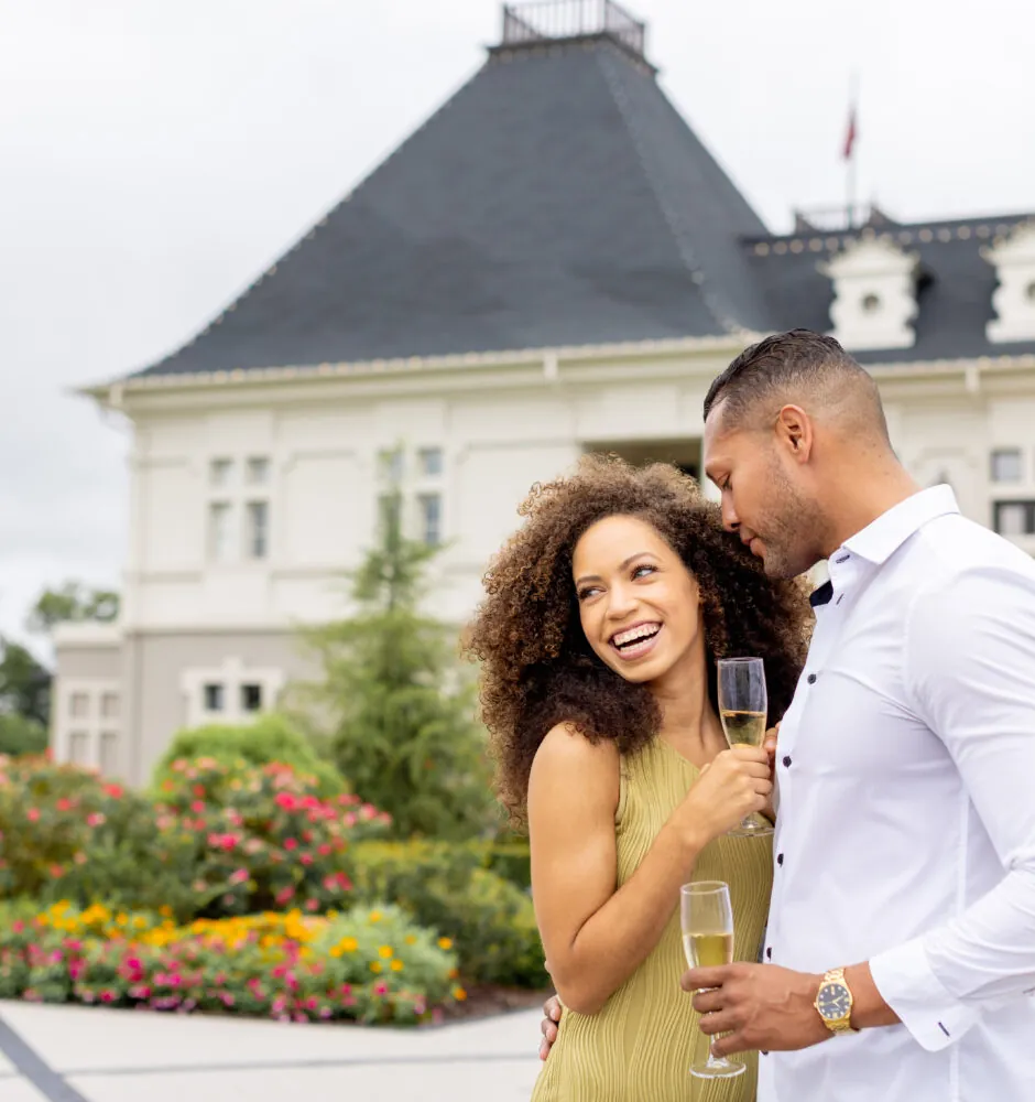 Smiling couple with champagne glasses in front of hotel