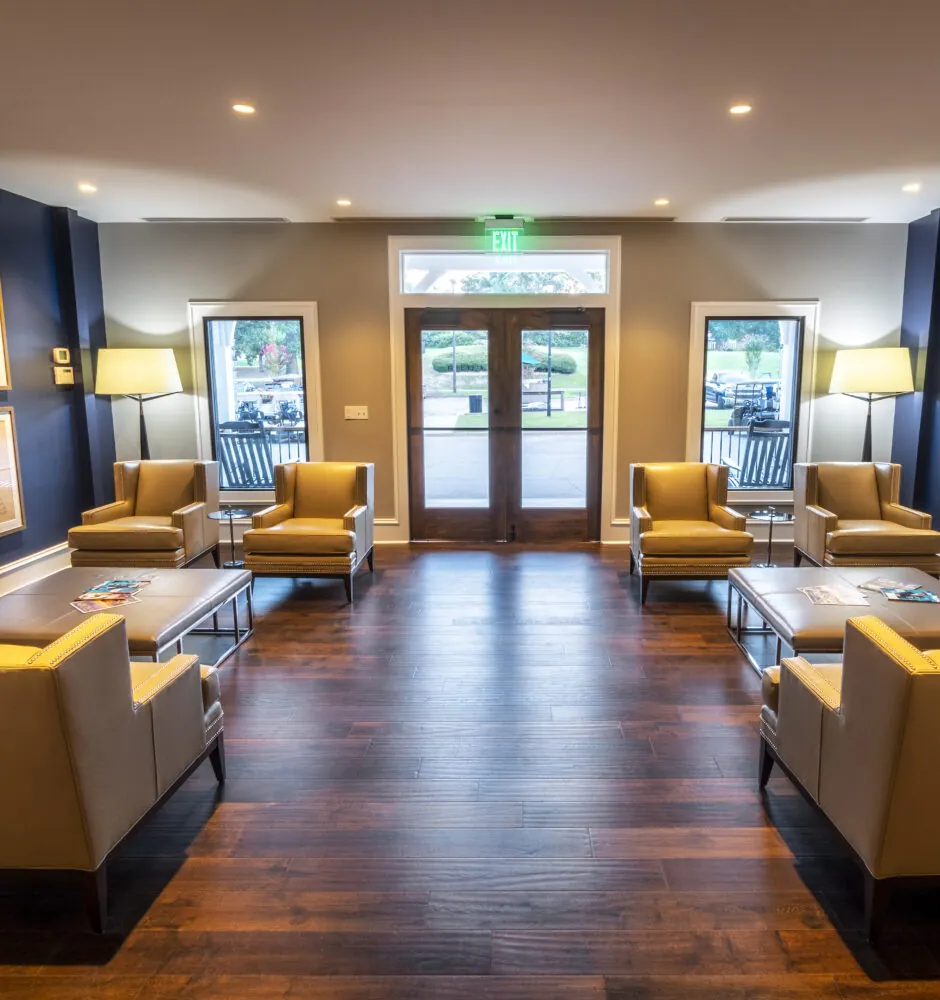 A long, narrow lounge area with dark blue walls, light-colored chairs, and two large landscape paintings on the walls. There are double glass doors at the far end of the room.