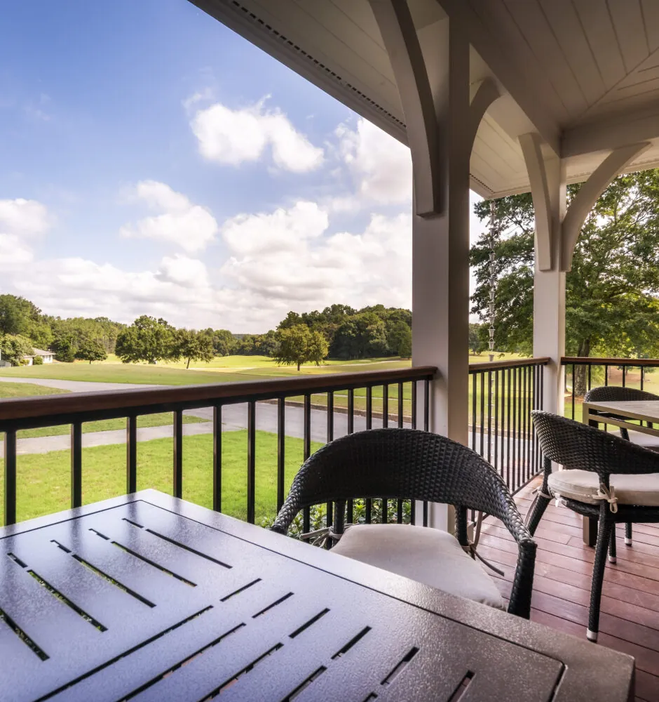 A porch with outdoor furniture overlooks a green golf course under a blue sky.