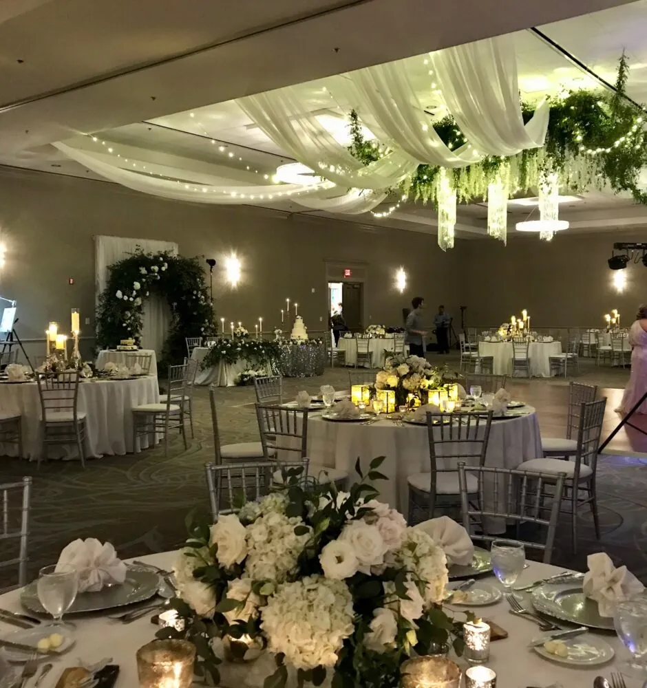 Wedding reception hall with draped fabric and chandeliers on the ceiling, and floral centerpieces on the tables.