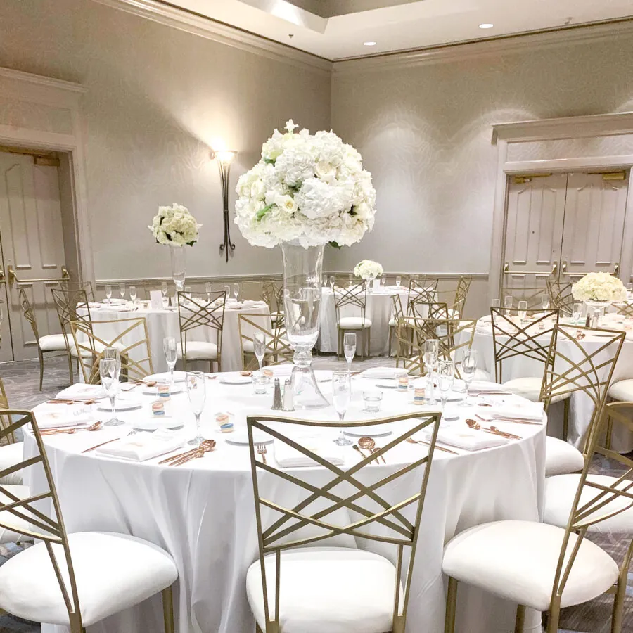 Round tables with white linens, gold chairs, and tall white floral centerpieces.