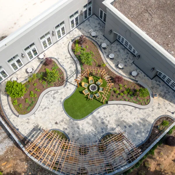 An aerial view of a modern courtyard with curving green spaces, a circular seating area, and a patterned wooden structure.