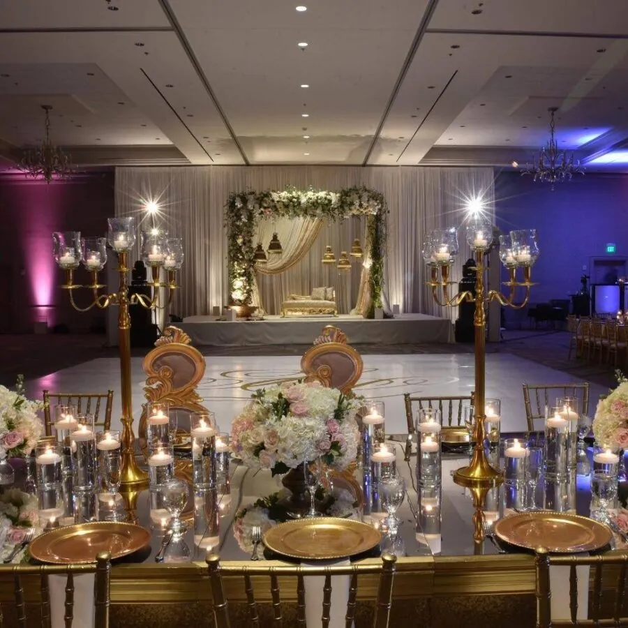 Wedding reception with long tables, candles, and pink and purple uplighting.
