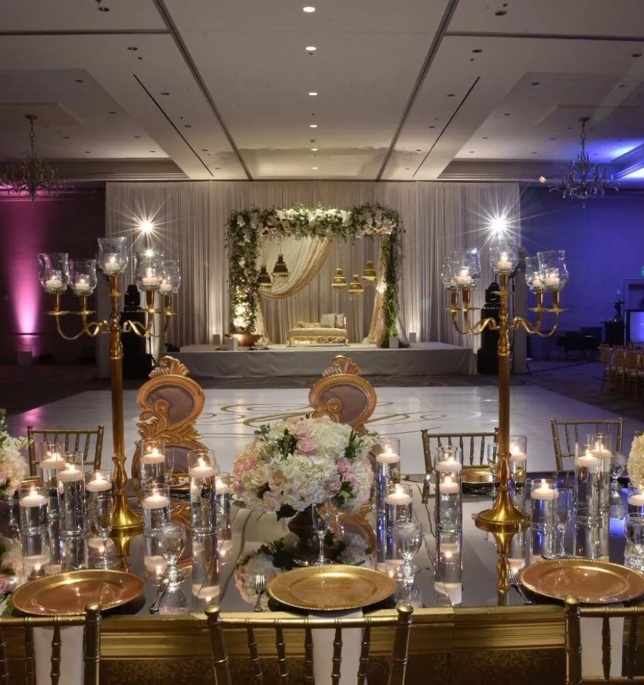 Wedding reception with long tables, candles, and pink and purple uplighting.