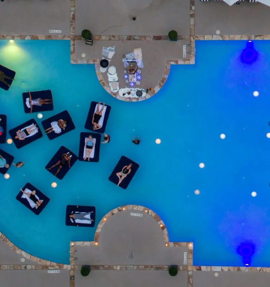 An aerial view of a swimming pool with multiple inflatable lounge floats shaped like cars.
